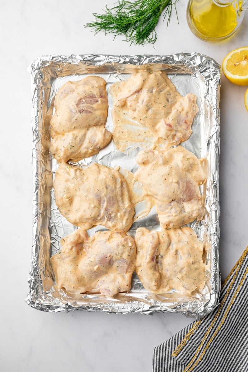 Yogurt marinated chicken thighs on a aluminum foil lined baking sheet.