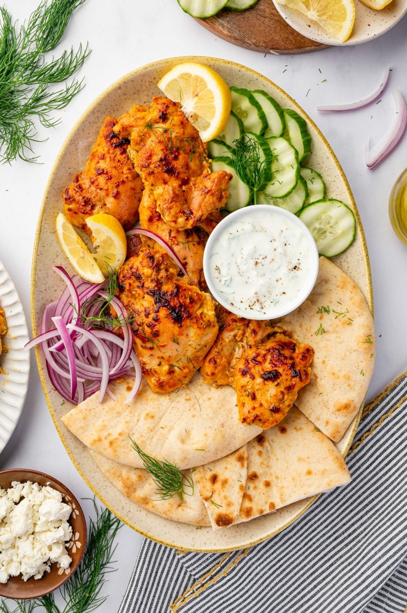 A platted filled with seasoned chicken thighs, cucumber, red onion, and pita.