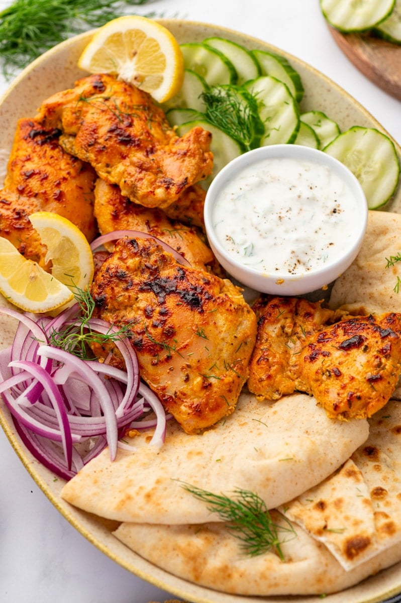 A platted filled with pita, cucumber, red onion, and seasoned chicken thighs.