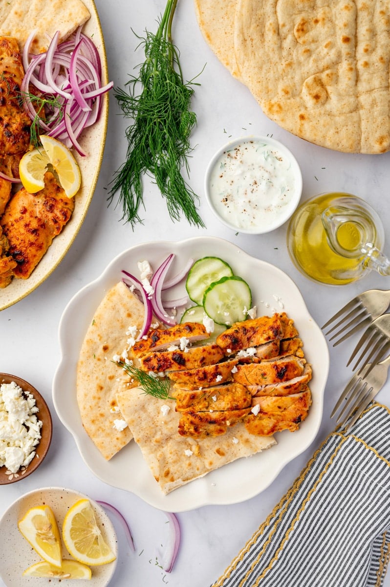 A plate with pita, vegetables, and sliced seasoned chicken thighs.