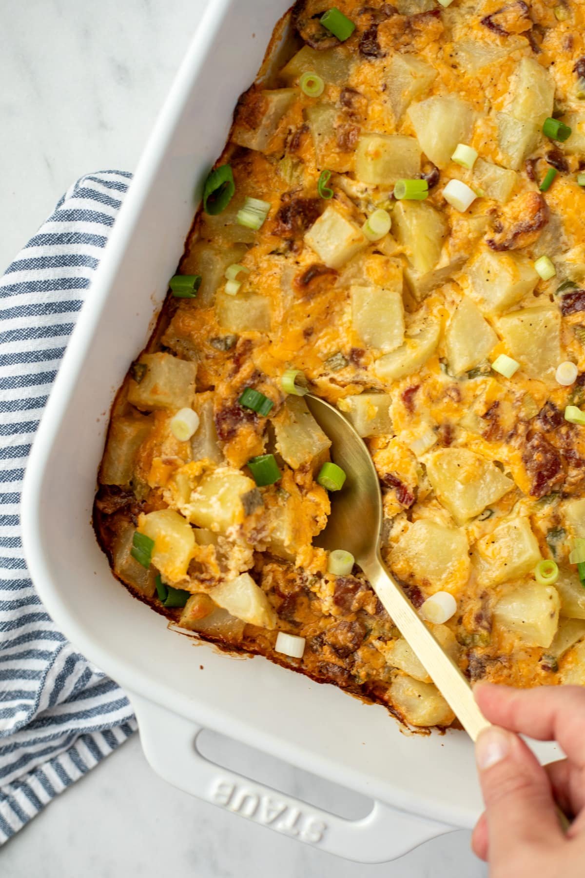 A spoon taking a portion of potatoes from a white baking dish.