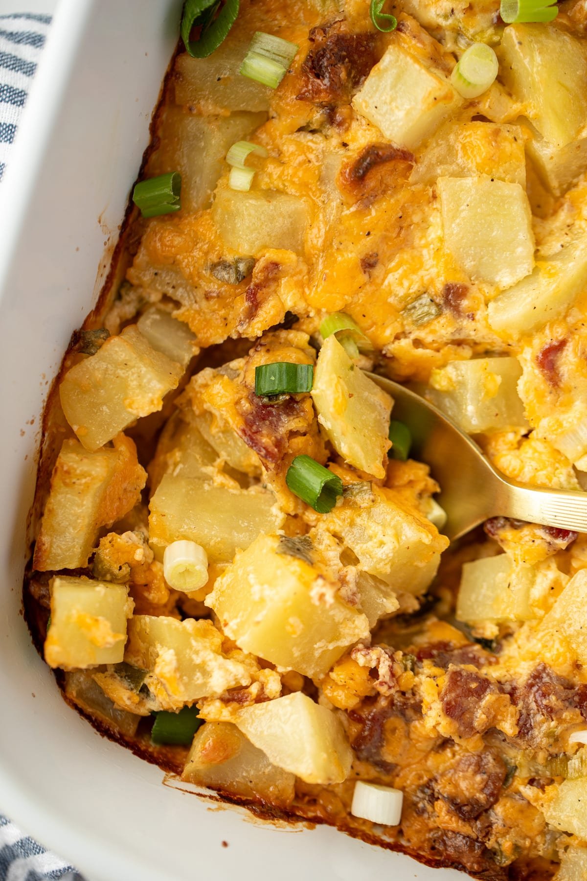 A spoon scooping into a potato casserole with cheese and bacon.