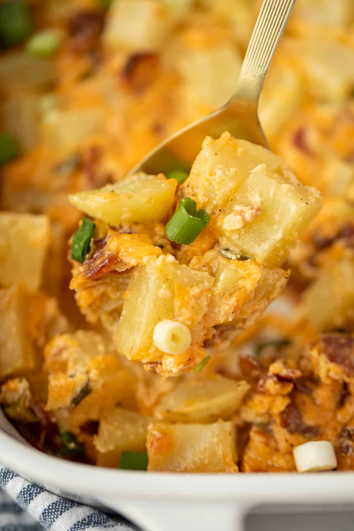 A spoonful of baked potato casserole dotted with green onion, cheese, and bacon.