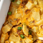 A spoon taking a portion of potato casserole from a baking dish.