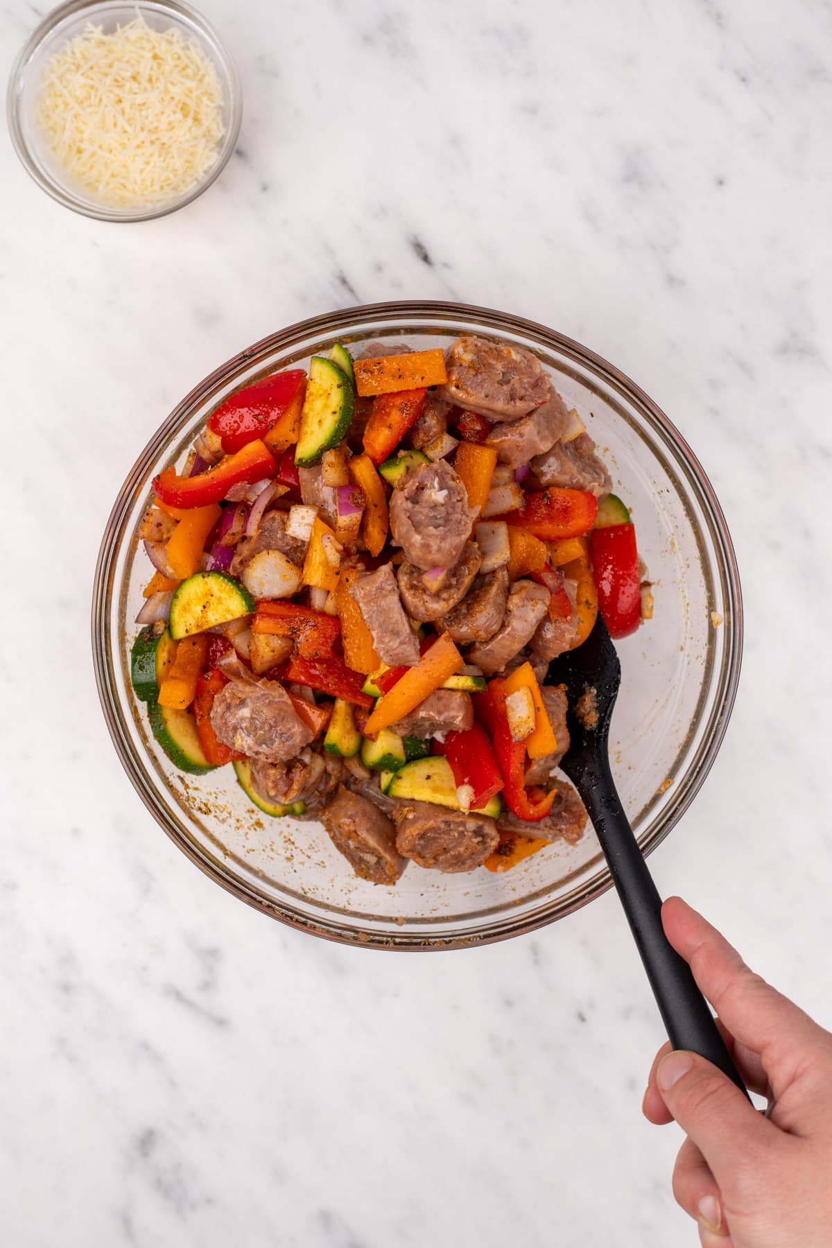 Stirring vegetables and sliced sausage together in a bowl.