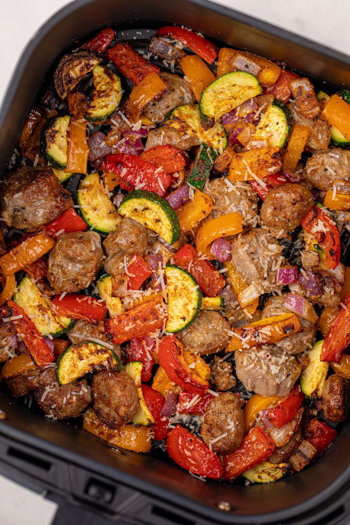 Cooked sausage chunks and vegetables in an air fryer basket.