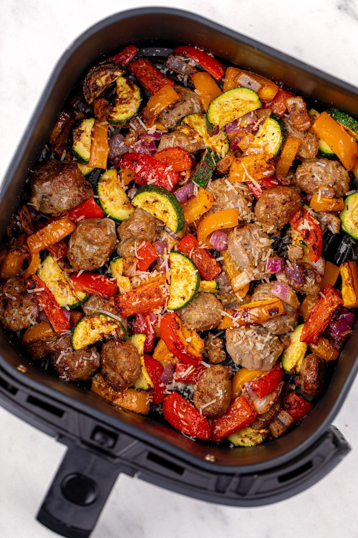 An air fryer filled with cooked chicken sausage and vegetables.