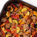 An air fryer basket filled with cooked vegetables and sausage slices.