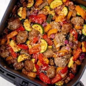Cooked sausage pieces and vegetables in an air fryer basket.