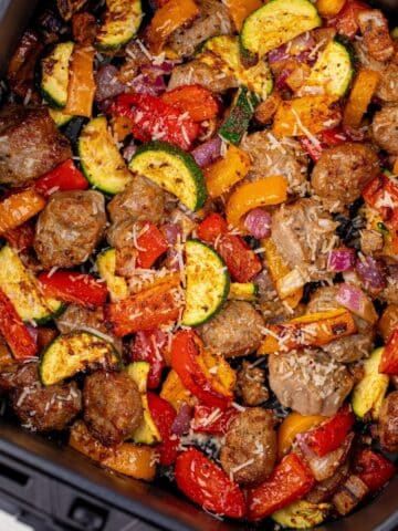 Cooked sausage pieces and vegetables in an air fryer basket.