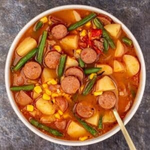 A bowl of hearty stew featuring sliced smoked sausage, potato, green bean, and corn.