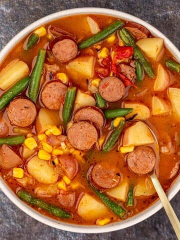 A bowl of hearty stew featuring sliced smoked sausage, potato, green bean, and corn.