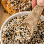 A small wooden spoon taking everything but the bagel seasoning from a bowl.