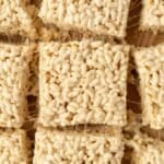 Rice cereal treats sliced into squares, resting on top of parchment paper.