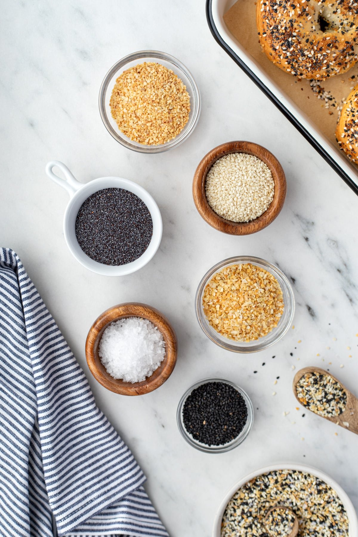 Small bowls of seasonings needed to make everything bagel seasoning, including poppy seeds, dried minced garlic, etc.