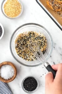 A small bowl of seeds and seasonings being mixed together with a small whisk.