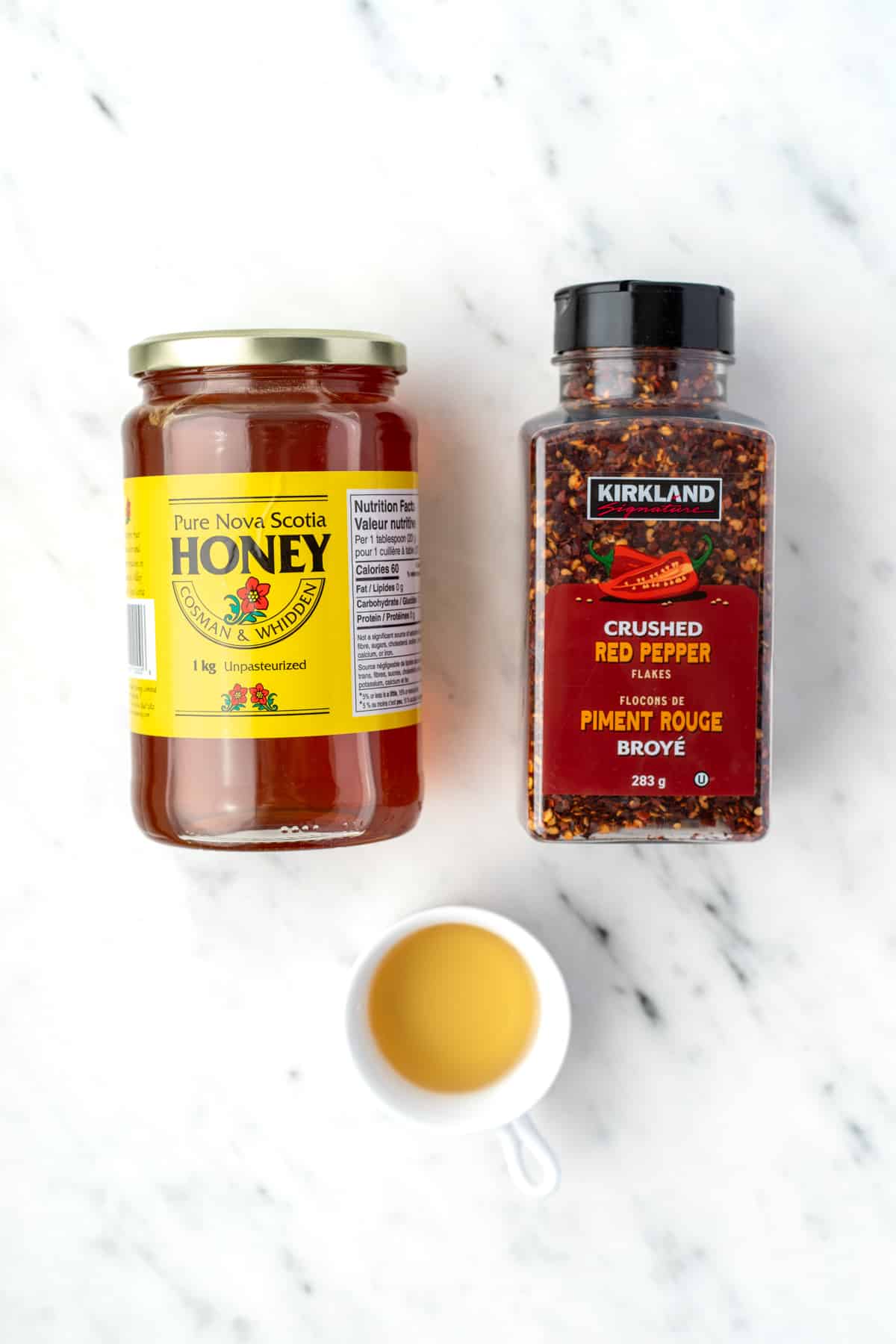 A jar of honey, a container of crushed chiles, and a small bowl of apple cider vinegar.