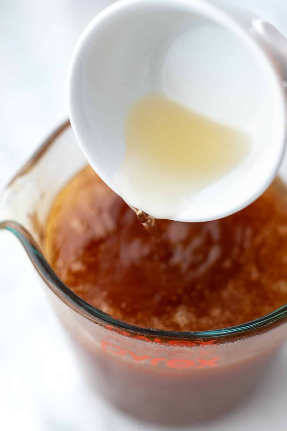 Pouring apple cider vinegar into a measuring cup full of honey.