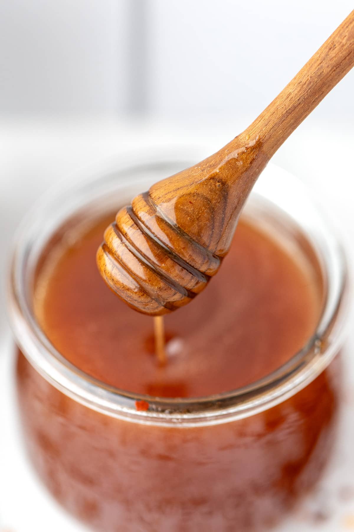 A honey dipper taking honey from a jar.