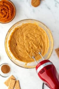 A bowl of pumpkin dip being whipped with an electric mixer.