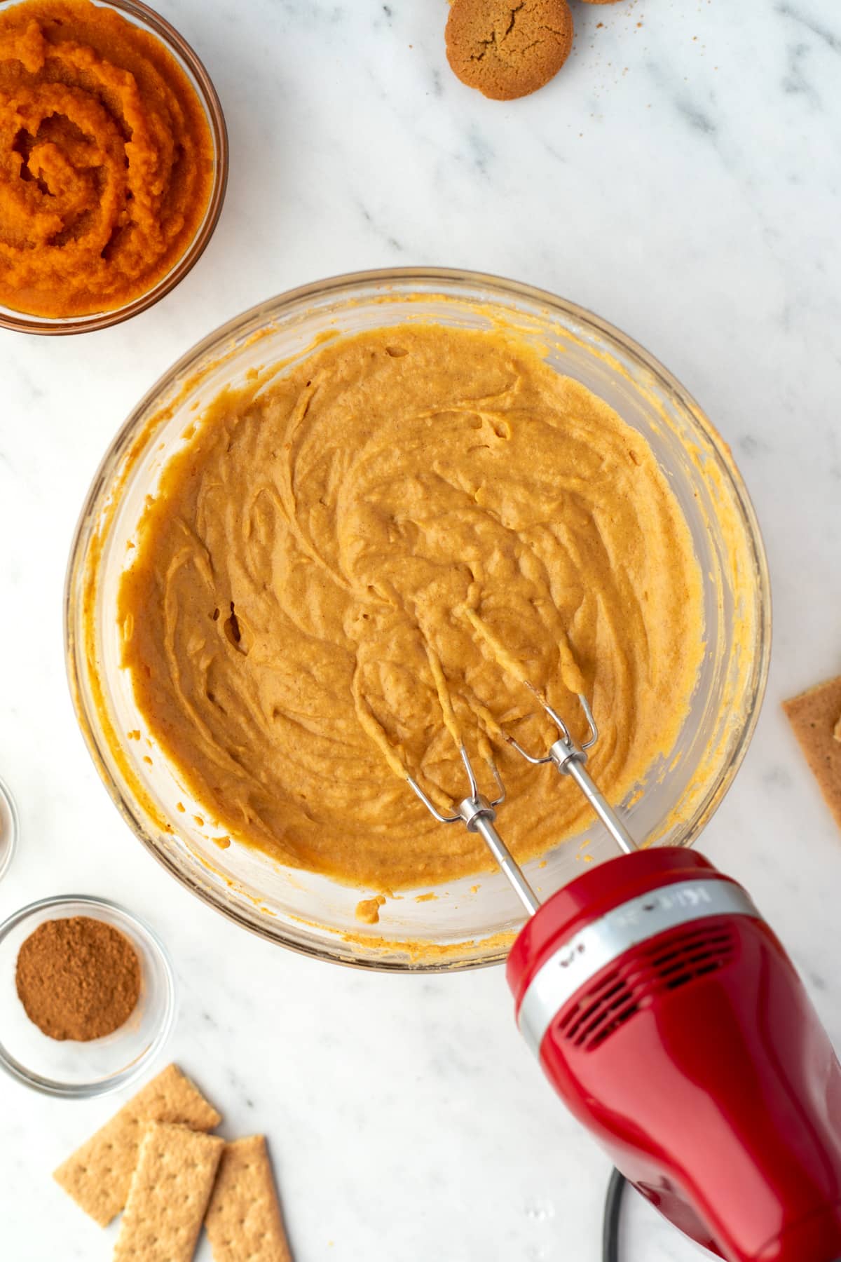 A bowl of pumpkin dip being whipped with an electric mixer.