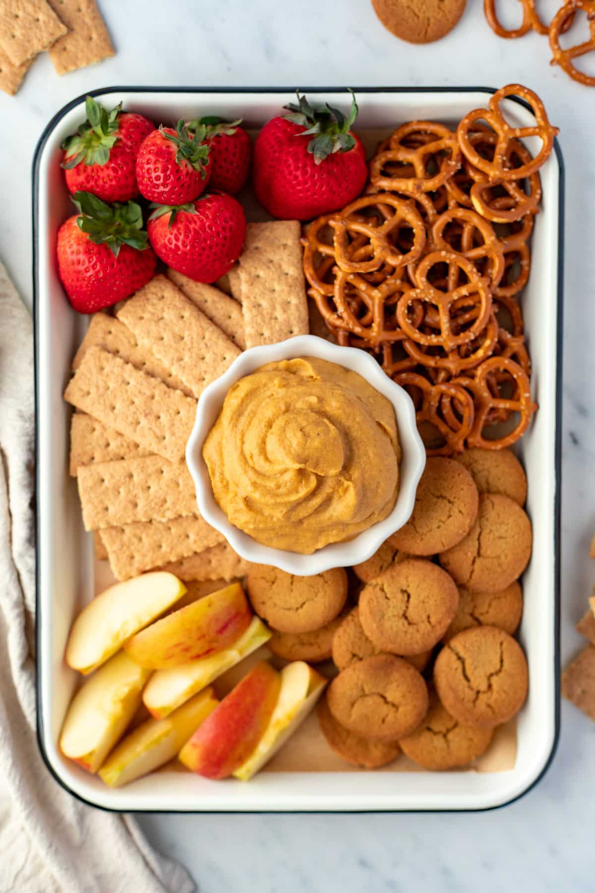 A tray filled with graham crackers, pretzels, apples, etc. with a bowl of pumpkin dip in the center.