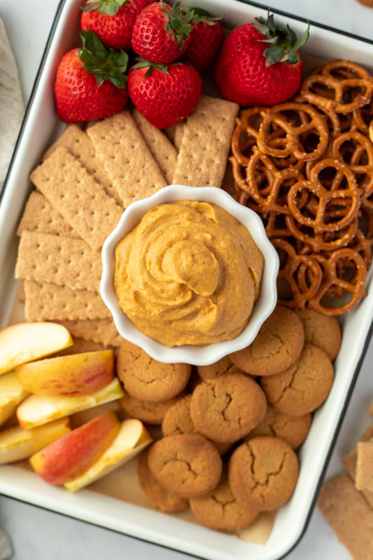 A tray filled with graham crackers, pretzels, fruit, and ginger snaps with a bowl of pumpkin dip in the center.