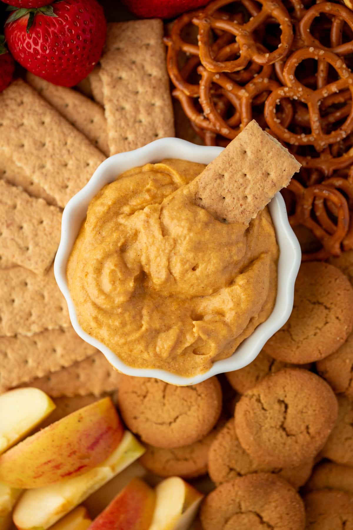 A graham cracker being dipped into pumpkin cheesecake dip.
