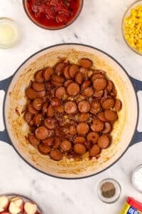 A dutch oven with lightly browned sliced smoked sausage in the center.