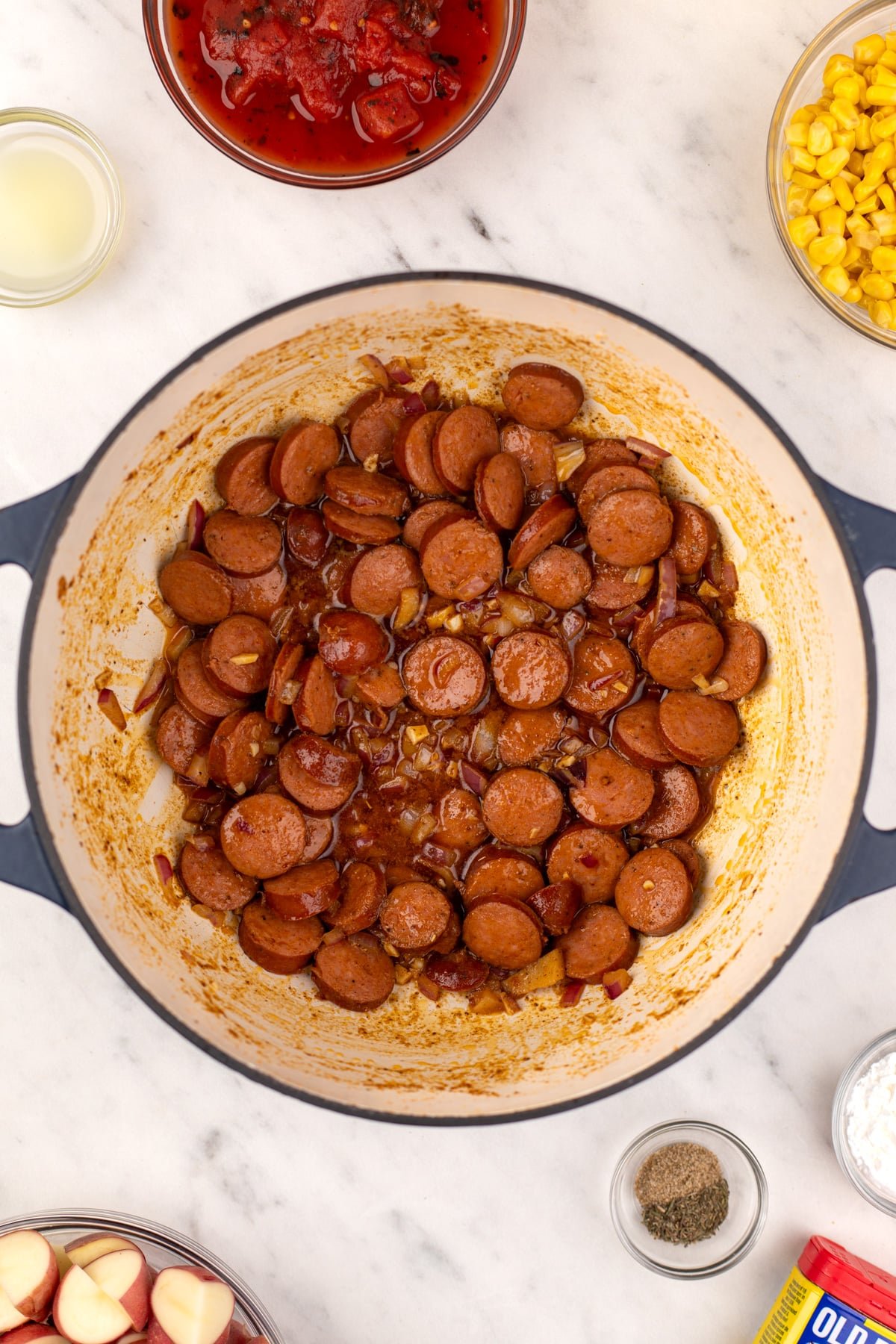 A dutch oven with lightly browned sliced smoked sausage in the center.