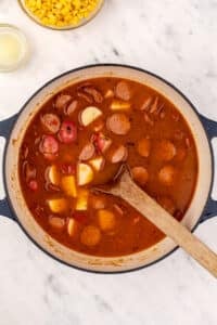 A dutch oven with soup inside, featuring chunks of potato and sliced smoked sausage.