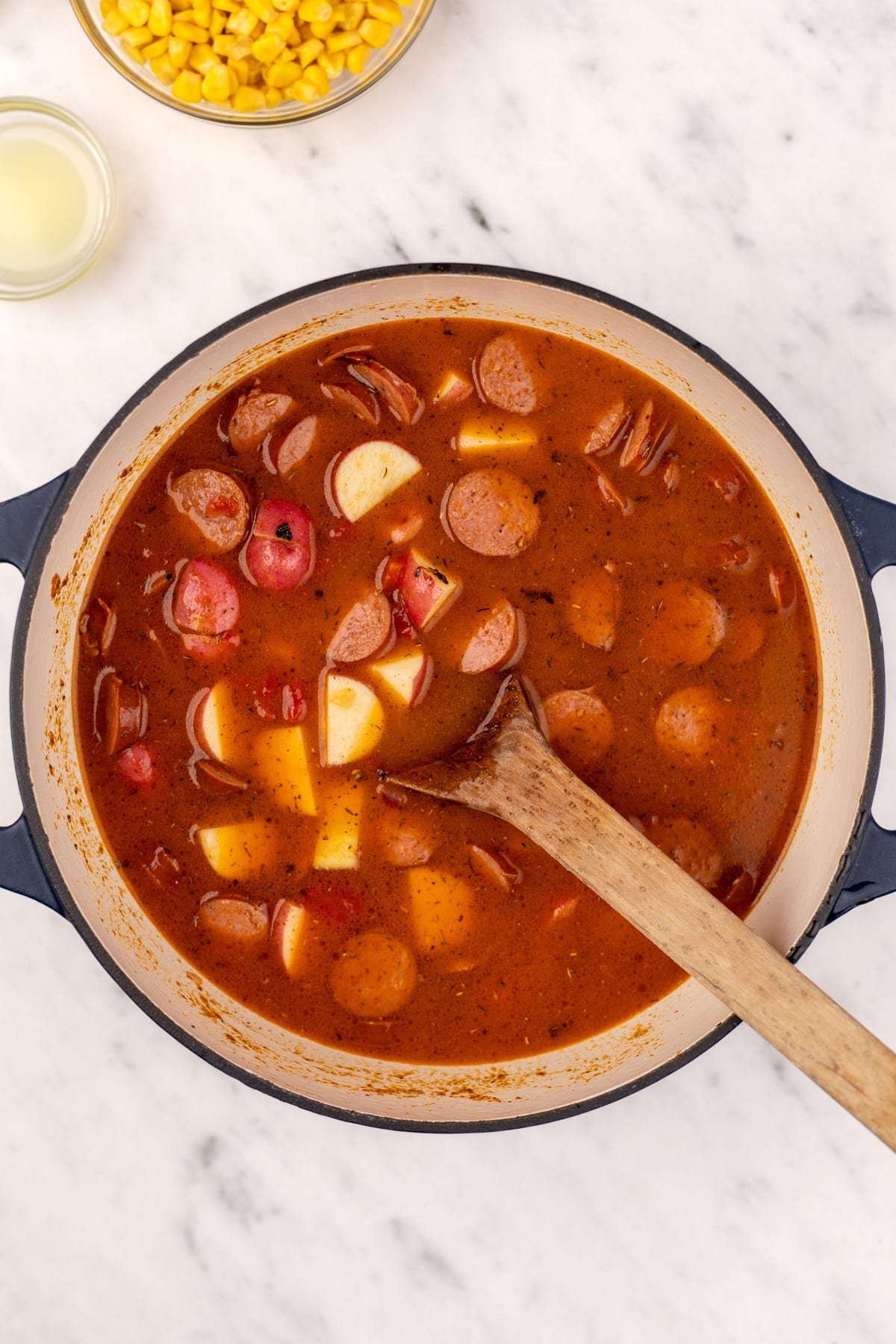 A dutch oven with soup inside, featuring chunks of potato and sliced smoked sausage.
