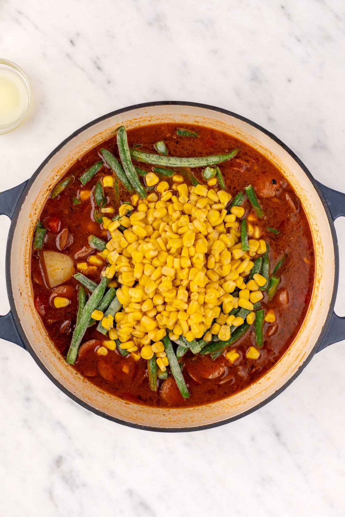 Adding frozen green beans and corn to a Dutch oven full of soup.
