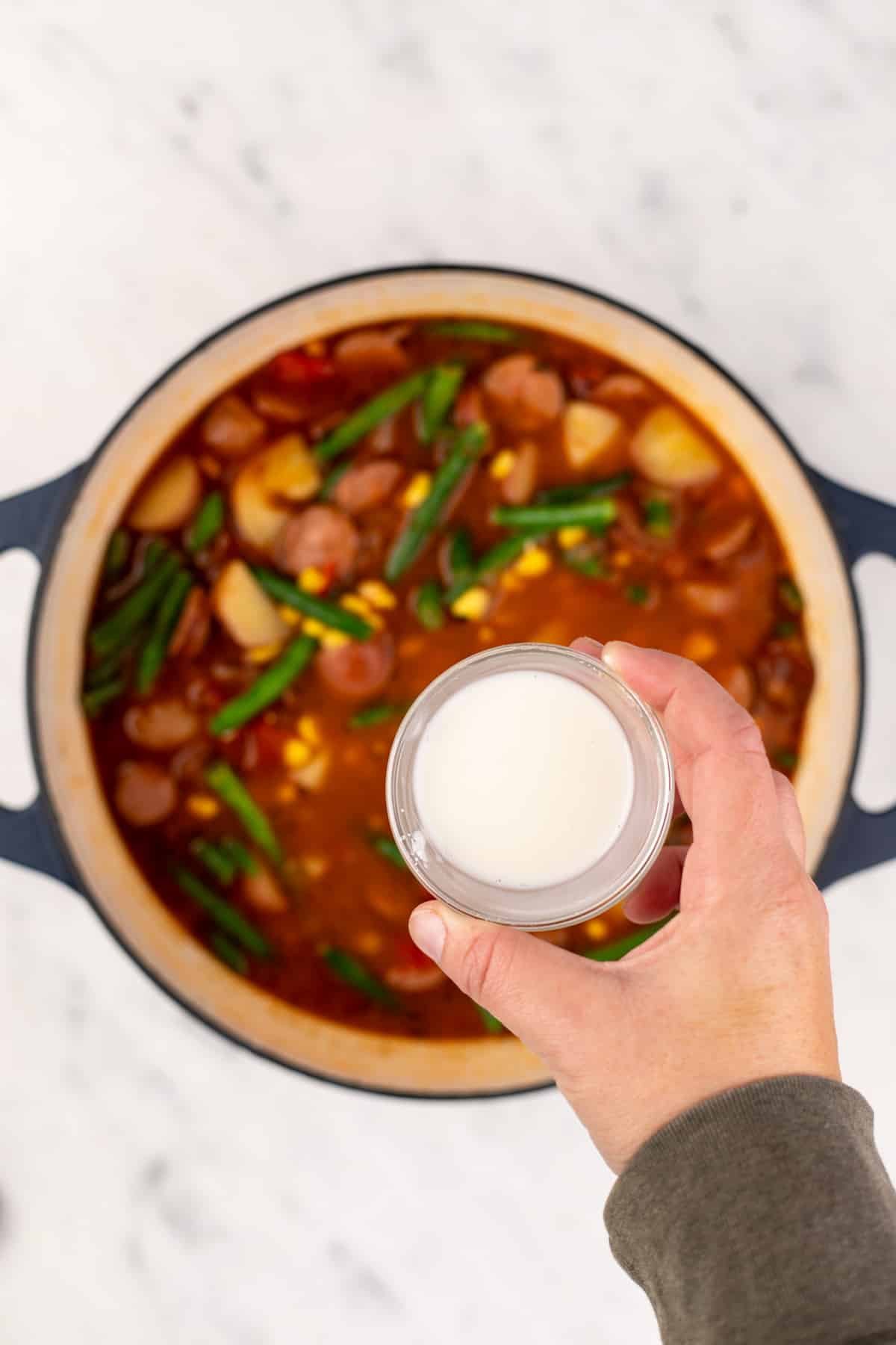 A small bowl of cornstarch hovering over a large Dutch oven full of soup.