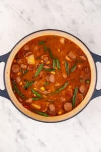 A large Dutch oven filled with a hearty tomato and broth-based soup.