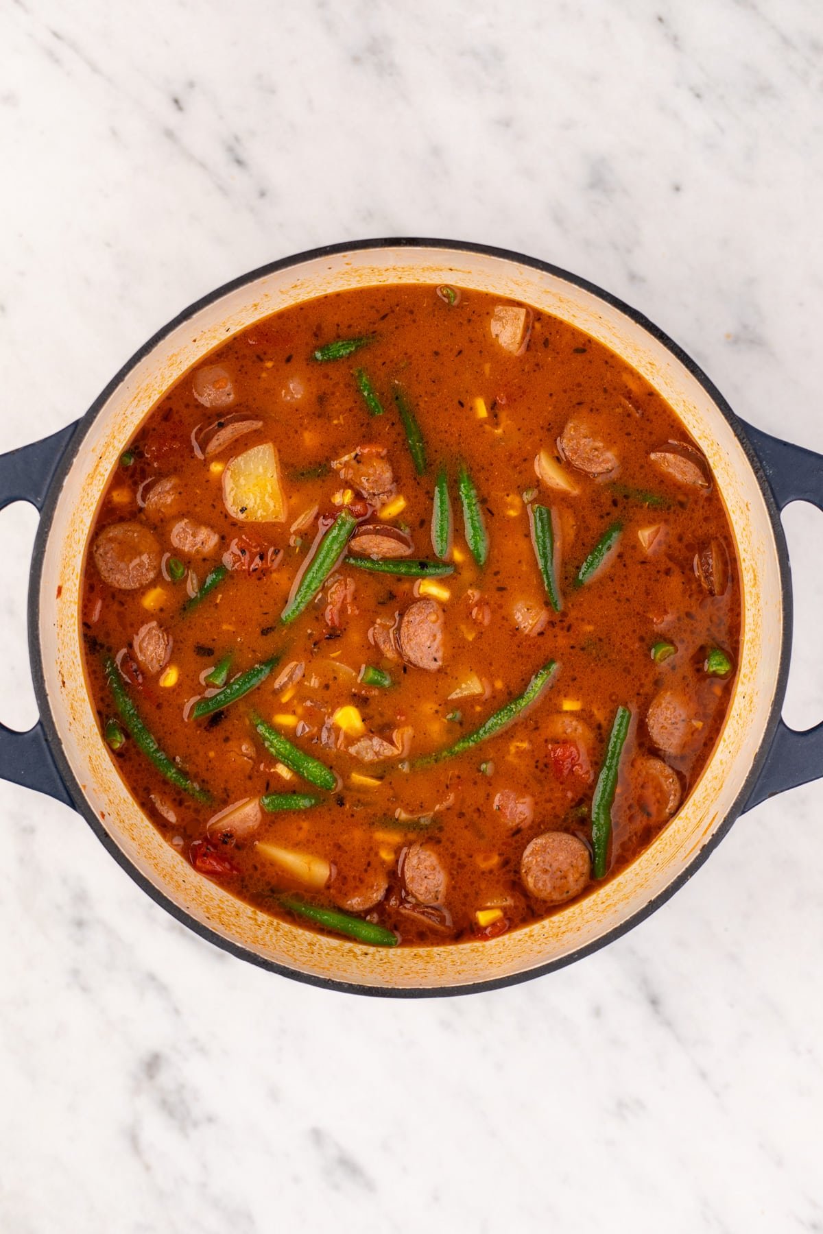 A large Dutch oven filled with a hearty tomato and broth-based soup.