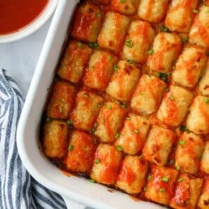 Tater tot chicken casserole in a baking dish topped with a drizzle of buffalo sauce.