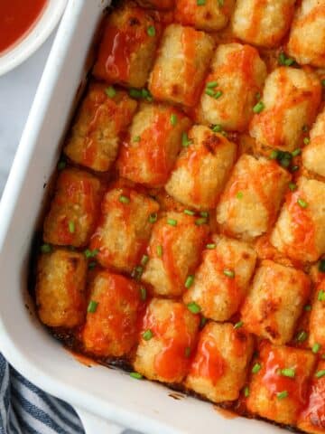 Tater tot chicken casserole in a baking dish topped with a drizzle of buffalo sauce.
