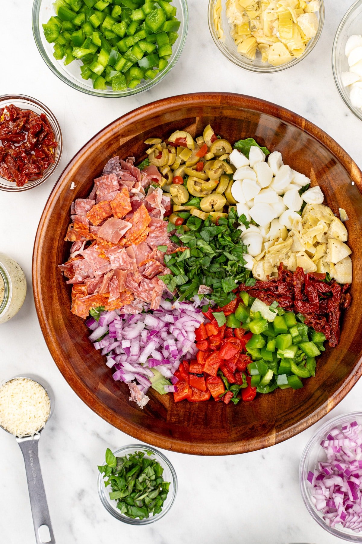 A salad bowl filled with a variety of toppings, including cheese, artichokes, sundried tomato, and chopped meats.