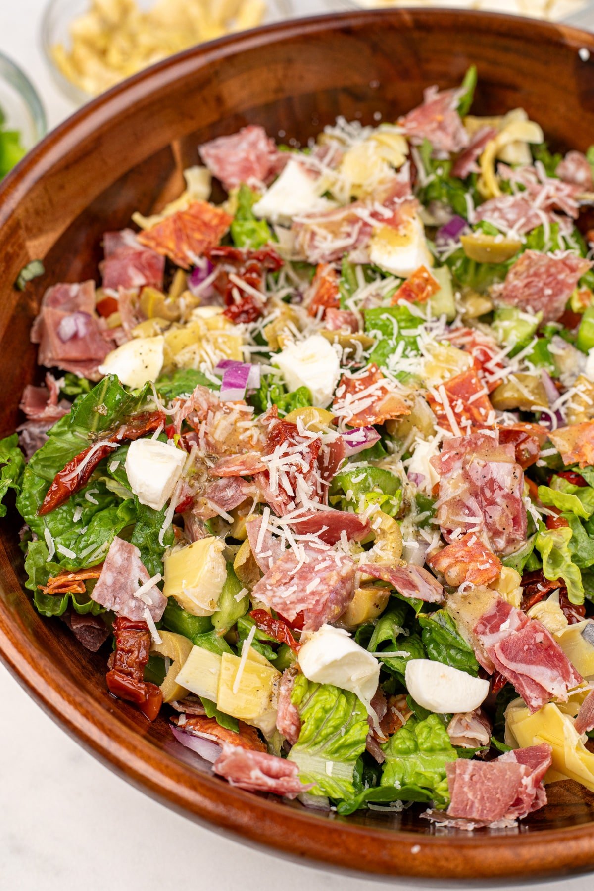A wooden salad bowl filled with chopped salad, featuring mozzarella balls, chopped meat, etc.