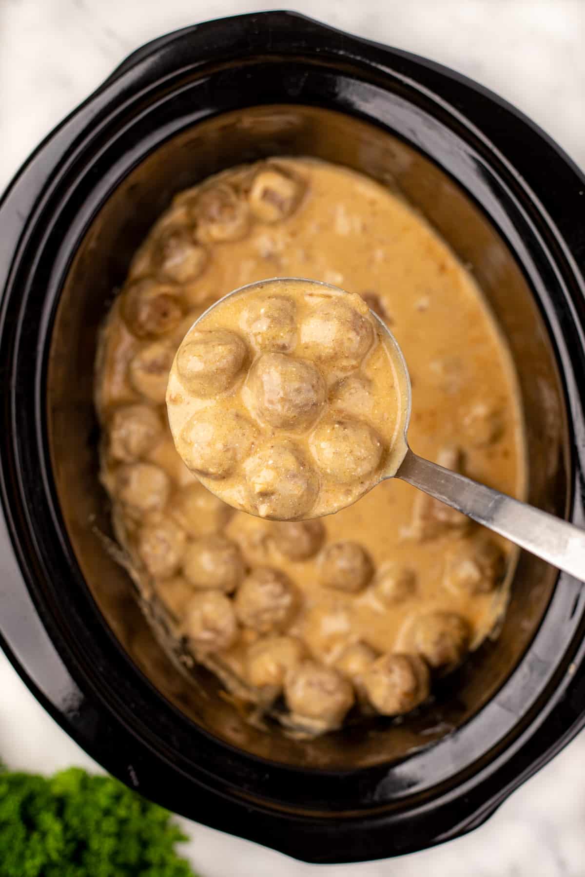 A ladleful of meatballs in a creamy sauce.
