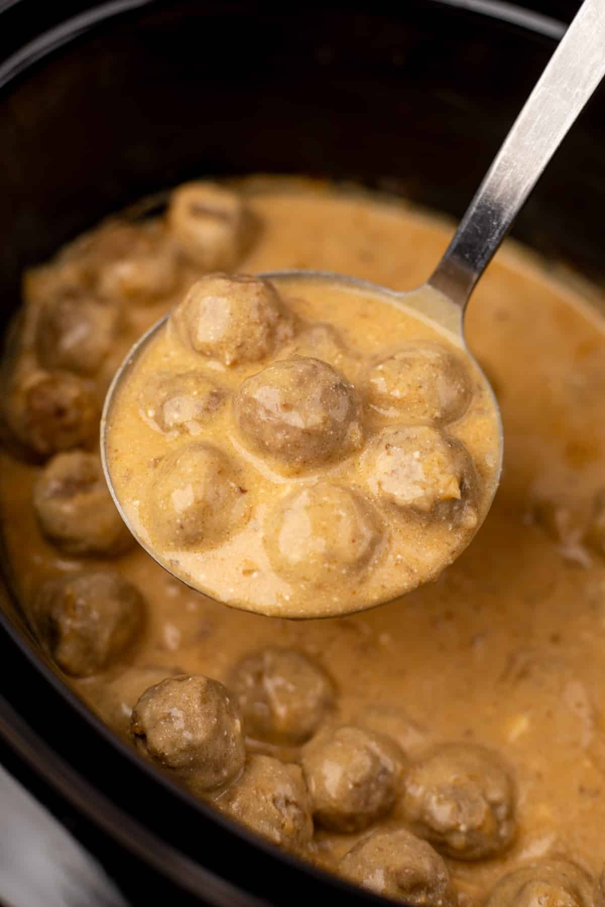 A ladle filled with creamy swedish meatballs being pulled from a slow cooker.