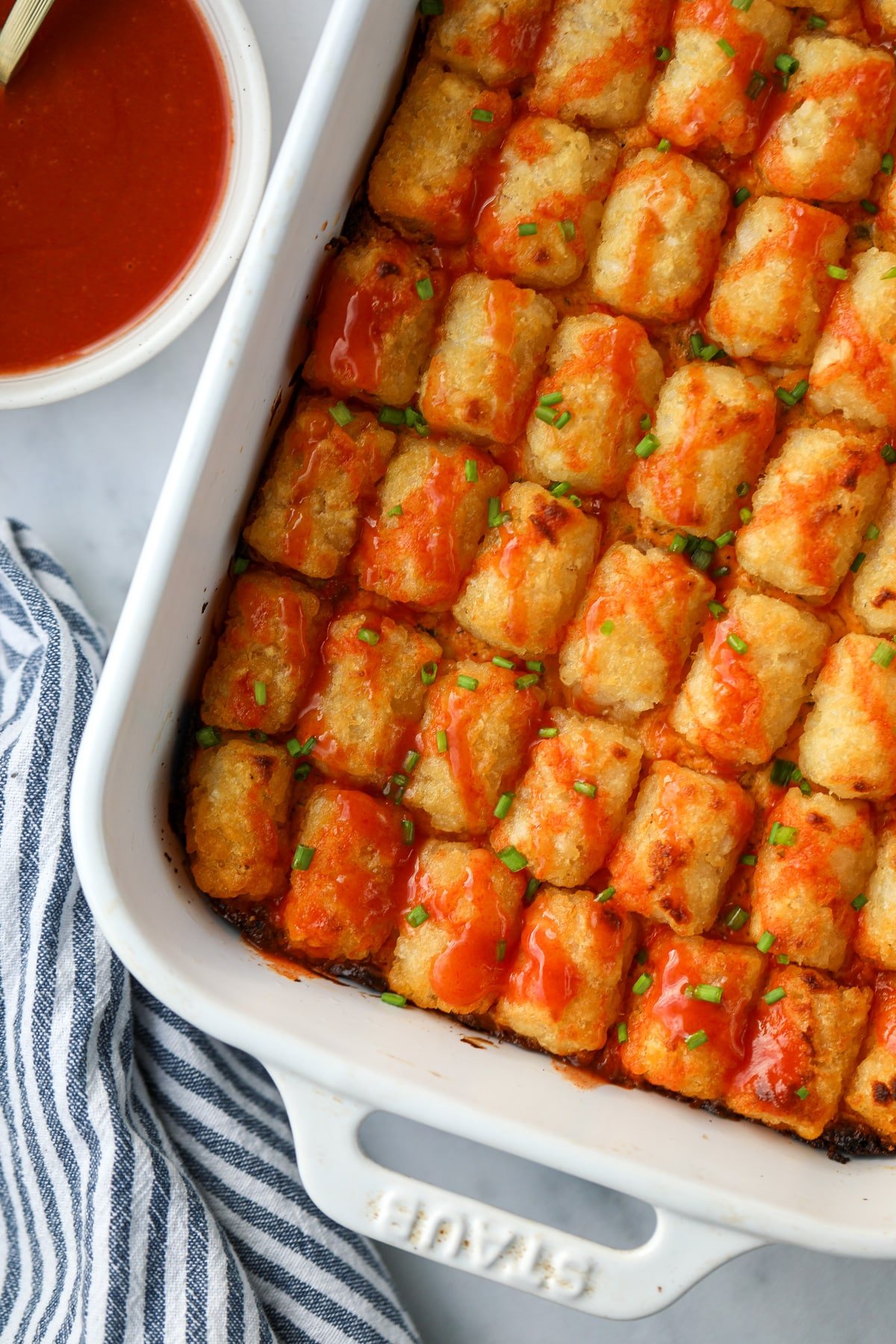 A baking dish filled with tater tot casserole topped with a drizzle of buffalo sauce.