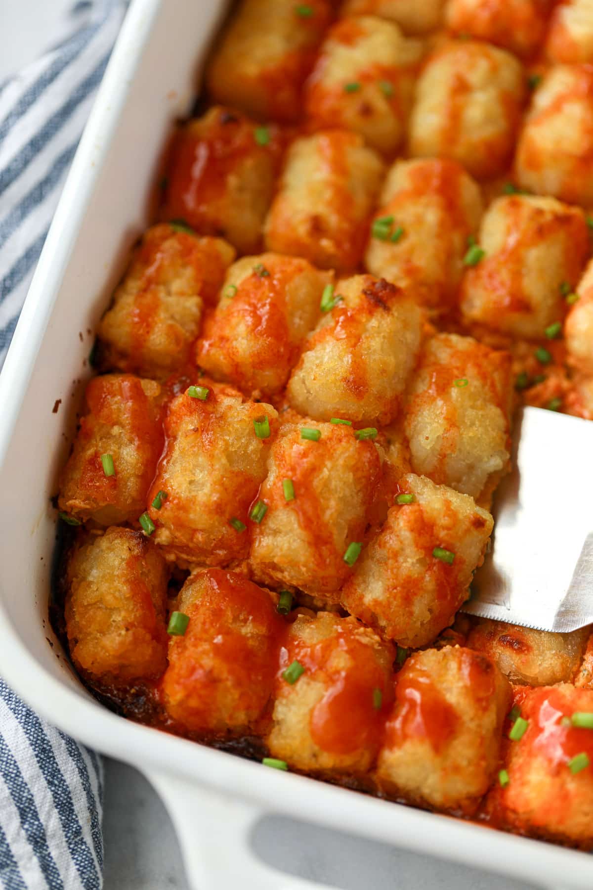 Using a spatula to remove a portion of tater tot casserole from a baking dish.