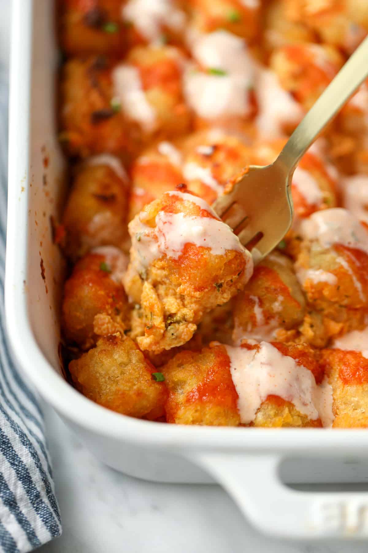 A fork holding up a small portion of buffalo chicken casserole drizzled with ranch dressing.