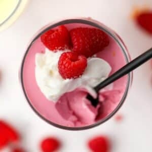 A small parfait glass filled with greek yogurt jello mousse, topped with whipped cream and raspberries.