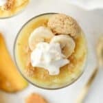 A pudding cup topped with banana slices, whipped cream, and vanilla cookies.