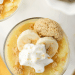 A small jar of banana pudding topped with whipped cream, banana slices, and cookie crumbs.
