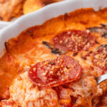 A spoon lifting a portion of pizza dip from a baking dish.