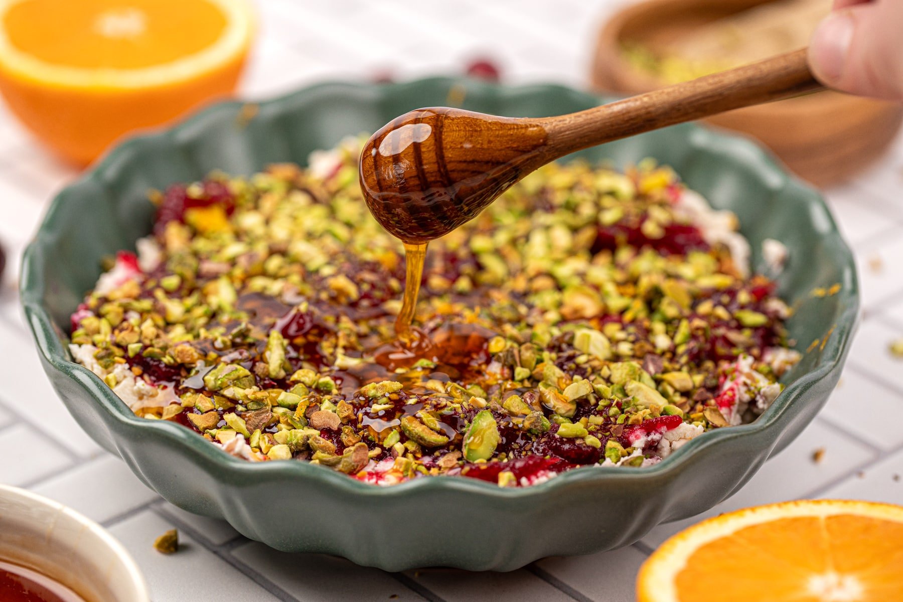 A honey dipper drizzling honey on top of a pistachio and cranberry dip.
